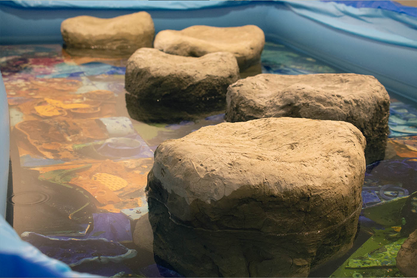 Detail of sculpture: ceramic tiles inside of a plastic pool, with water.
