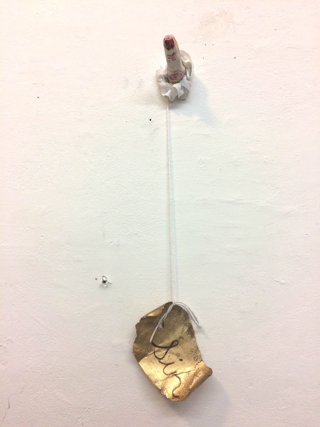 Installation view, sculpture of finger mounted on wall with tangling note with the word Sin written on it.
