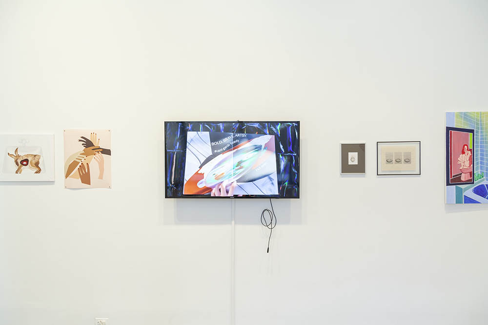Exhibition view of works on paper and a video monitor mounted on the wall.
