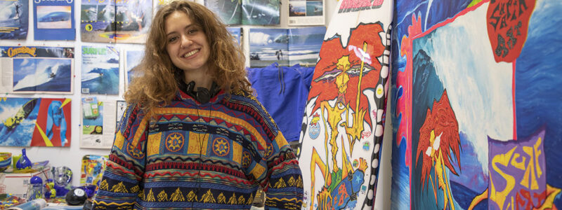The artist in their studio with many surf themes images in the background.