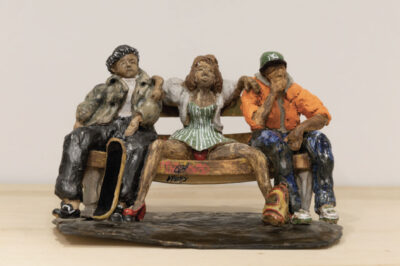 Clay sculpture of three figures seated on a bench.
